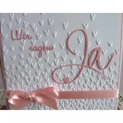 Einladungskarte zur Hochzeit in weiß/rosa, mit geprägtem Hintergrund, und *Wir sagen Ja* Schriftzug