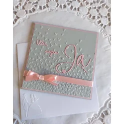 Einladungskarte zur Hochzeit in grau/rosa, mit geprägtem Hintergrund, und "wir sagen Ja" Schriftzug