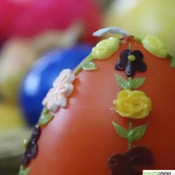 große Ostereikerze in orange mit doppelter, frühlingshafter Blumenranke verziert, Osterdeko, Ostergeschenk